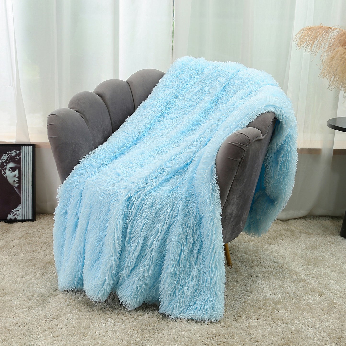 Light blue fluffy blanket draped over a gray armchair in a room with white curtains.