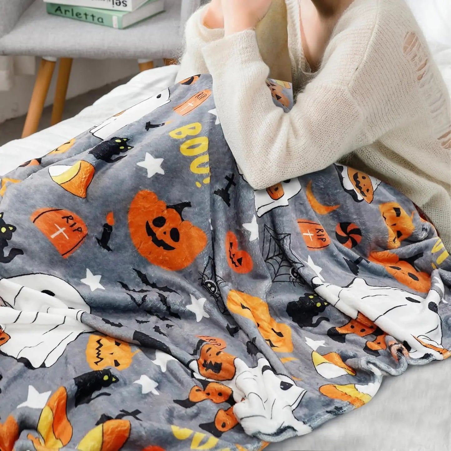 Soft grey Halloween throw blanket with white ghosts and yellow pumpkins on a cozy bed setup